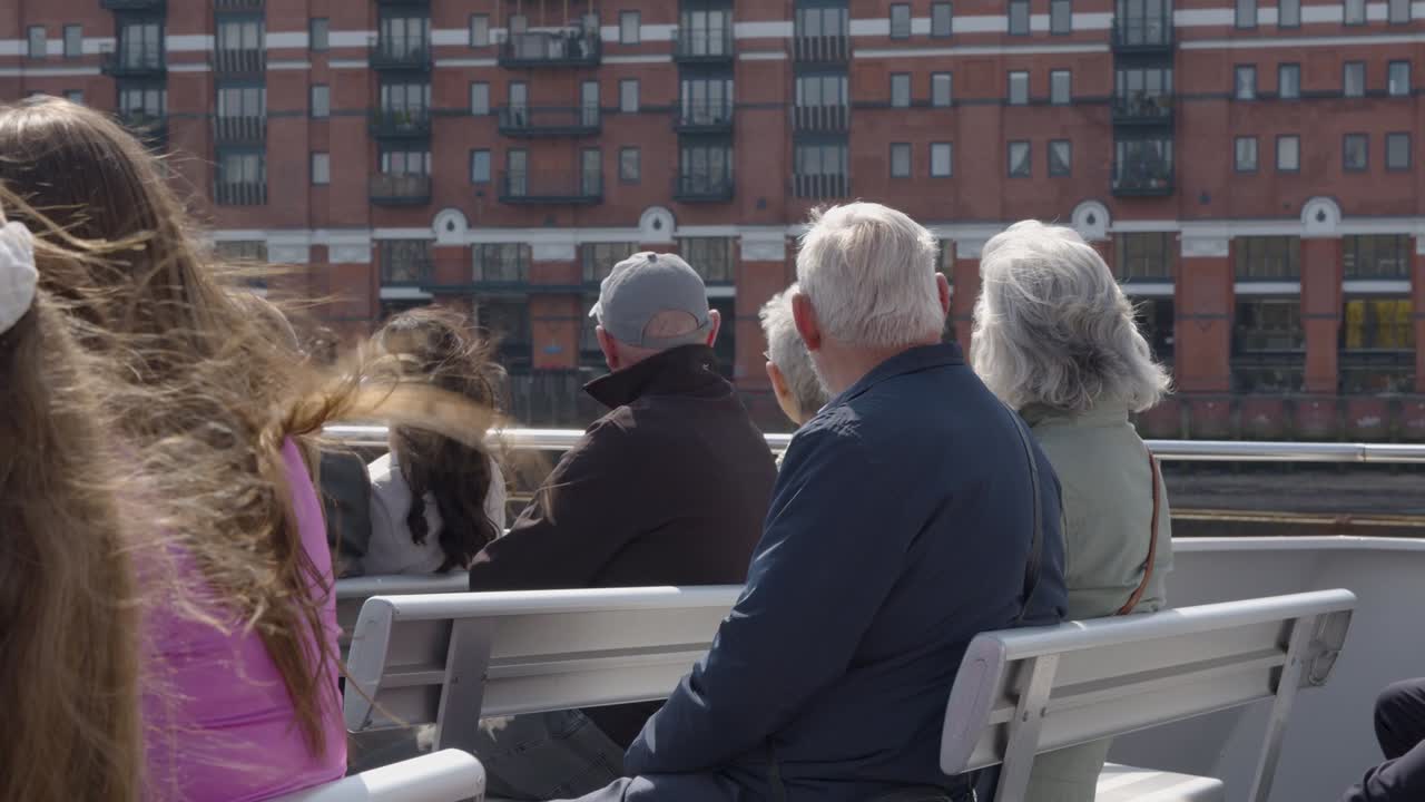 테임즈 강 에 있는 보트 에 앉아 있는 관광객 들 이 런던 시의 스카이라인 에 있는 건물 들 을 지나가고 있다
