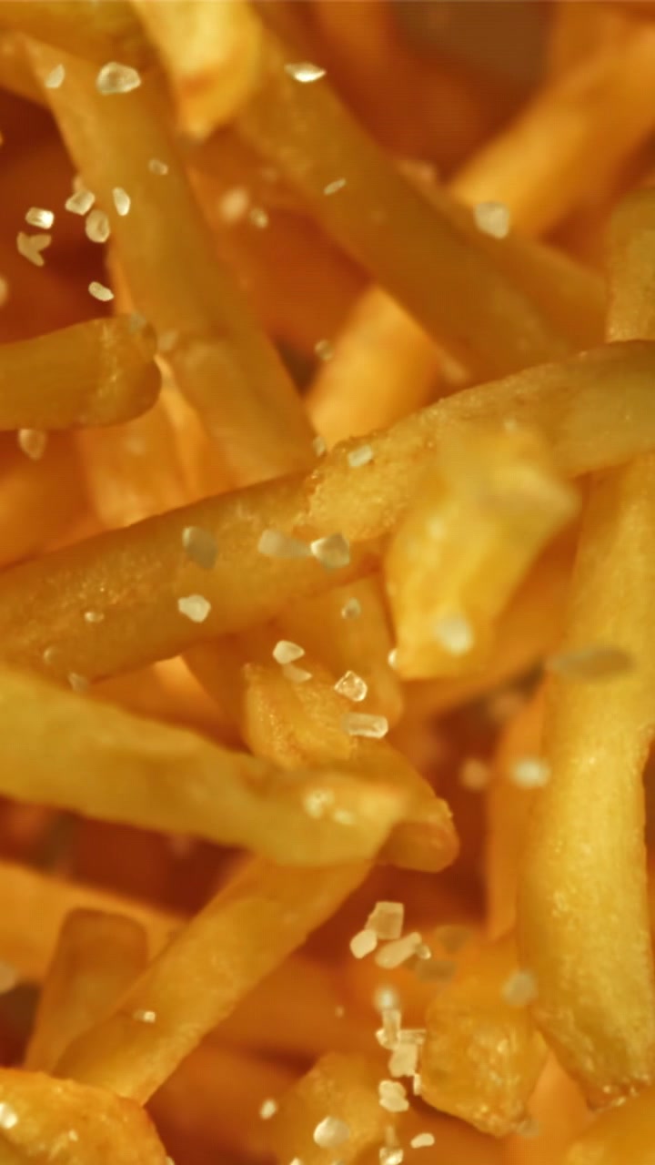 Close-up of Salt Crystals Falling onto Golden French Fries
