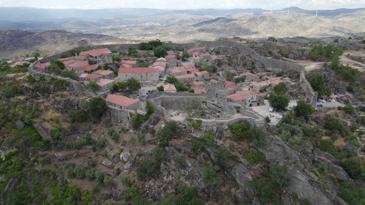 Vista orbitale di case in pietra in un villaggio all'interno delle mura di fortificazione, su una collina verdeggiante, Sortelha