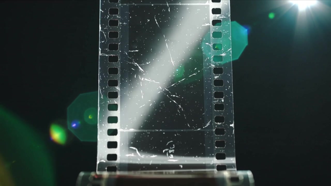 Unwinding film strip with sprockets sliding in studio with diagonal beam, showing canister and dust