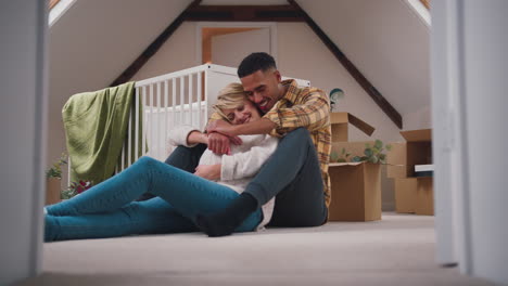 loving couple expecting baby hugging in nursery of new home together with moving in boxes