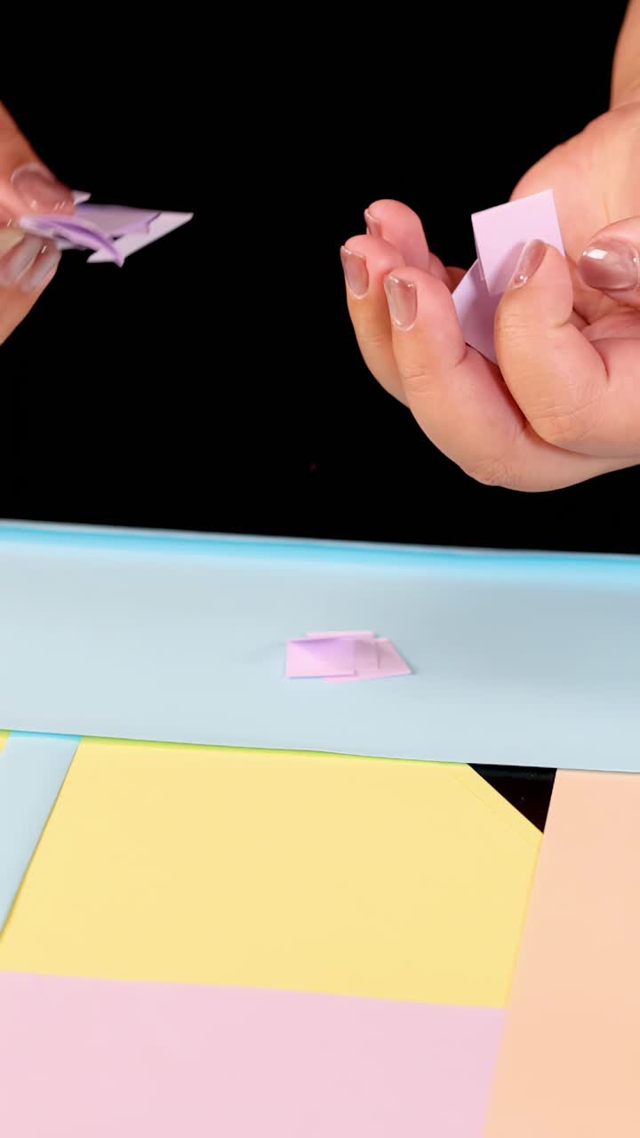 Mani di bambino raccolgono piccoli ritagli di carta per lavoretti su un tavolo color pastello sotto un'illuminazione brillante e uniforme.