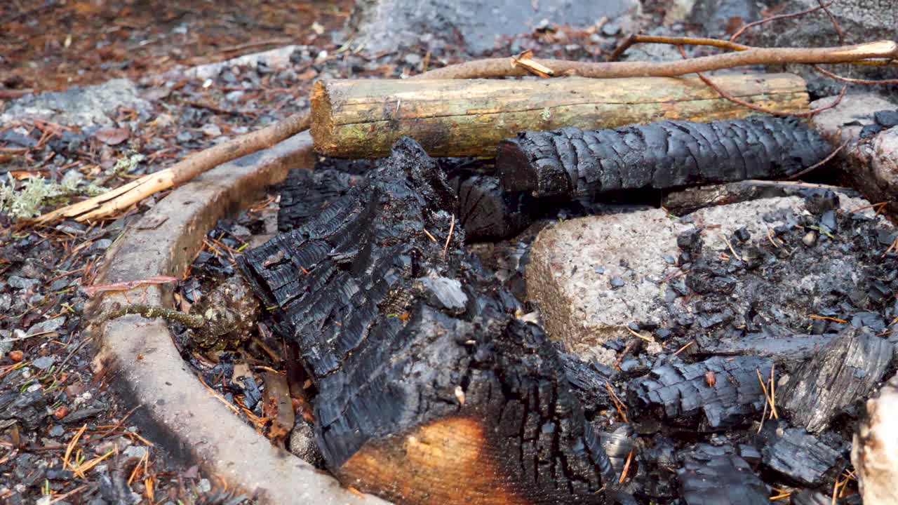 A burnt out or extinguished campfire at a campground fire pit the morning after on a cold, wet day