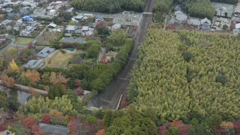 Sagano-scenic-train-at-Torokko-station-and-Arashiyama-bamboo-grove,-Aerial-Pan