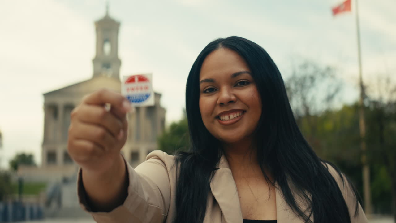 Woman holding 'I Voted' sticker in front of government building