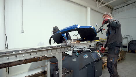 vinnytsia, ukraine - january 19, 2023: automatic band saw machine cutting metal rod with water base cooling method. worker near machine tool for industrial purpose