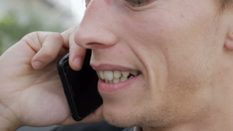 primer plano de un joven hablando por teléfono afuera, pareciendo emocionado