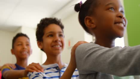 Multi-ethnic-school-kids-standing-in-row-with-their-hands-on-shoulder-in-classroom-4k