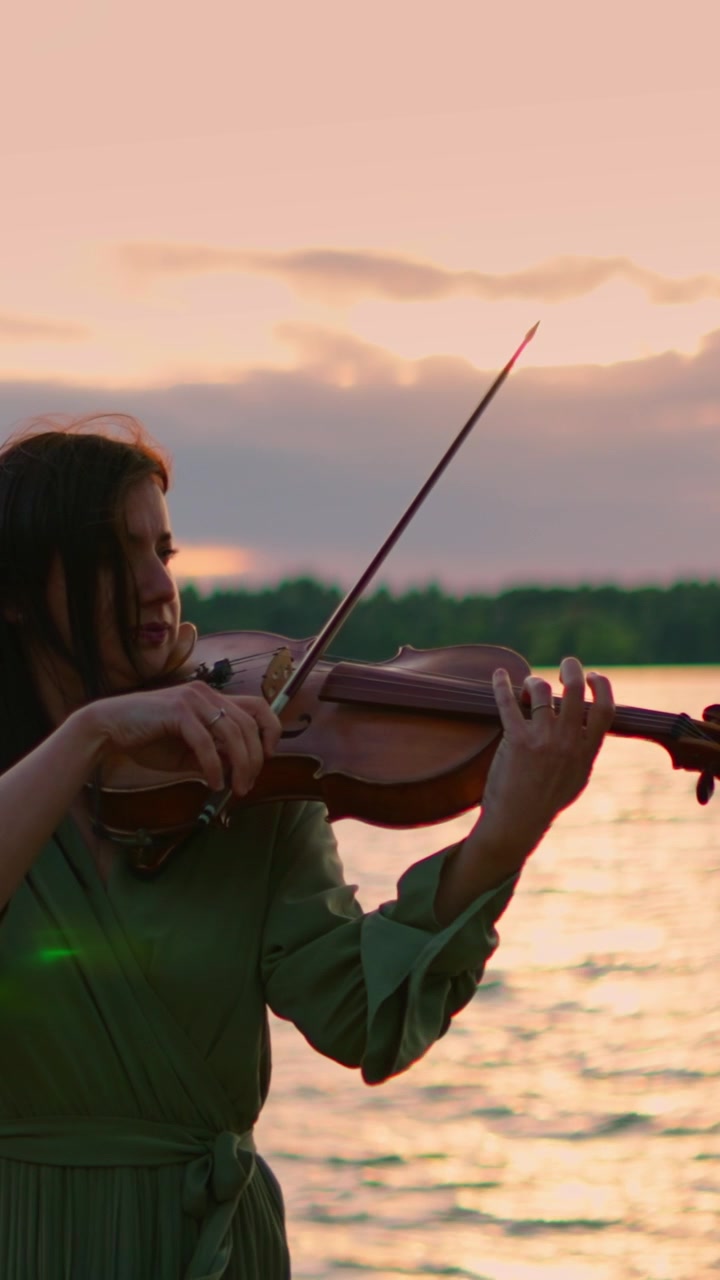 Young Woman Playing Violin by the Lake at Sunset