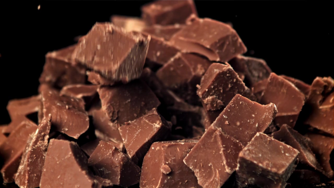 Pezzi di cioccolato al latte che cadono al rallentatore su sfondo nero
