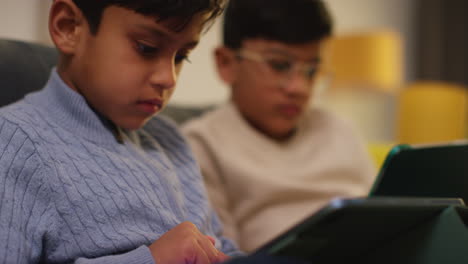 two young boys sitting on sofa at home playing games or streaming onto digital tablets 15