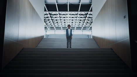 Lonely pupil standing empty hallway on stairs alone. Schoolboy feeling stressed.