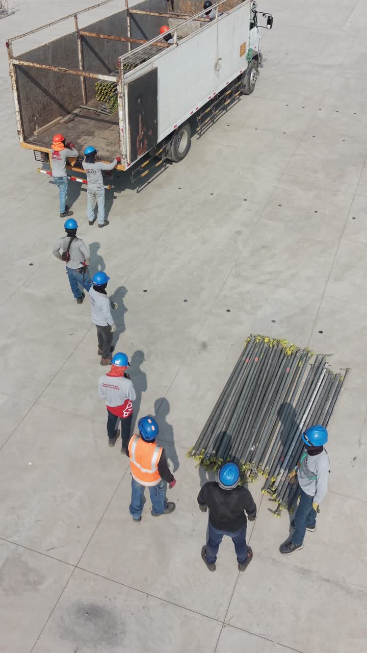 Construction Workers Unloading Scaffolding Pipes from Truck in Human Chain