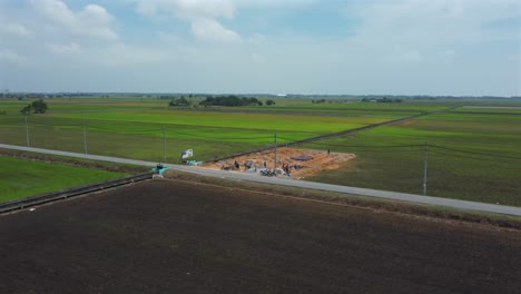 construction work going on near green paddy fields, aerial point of interest shot