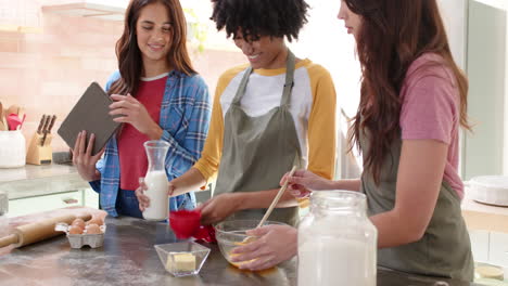 women friends baking together in kitchen, using tablet for recipe guidance, smiling warmly