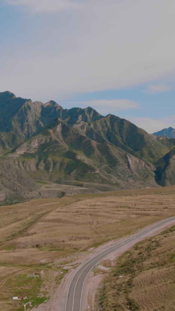 Veduta aerea della strada Chuysky Trakt che si snoda attraverso un'ampia valle montana con creste verdi e un paesaggio di steppa aperta nella Repubblica dell'Altai, Russia.