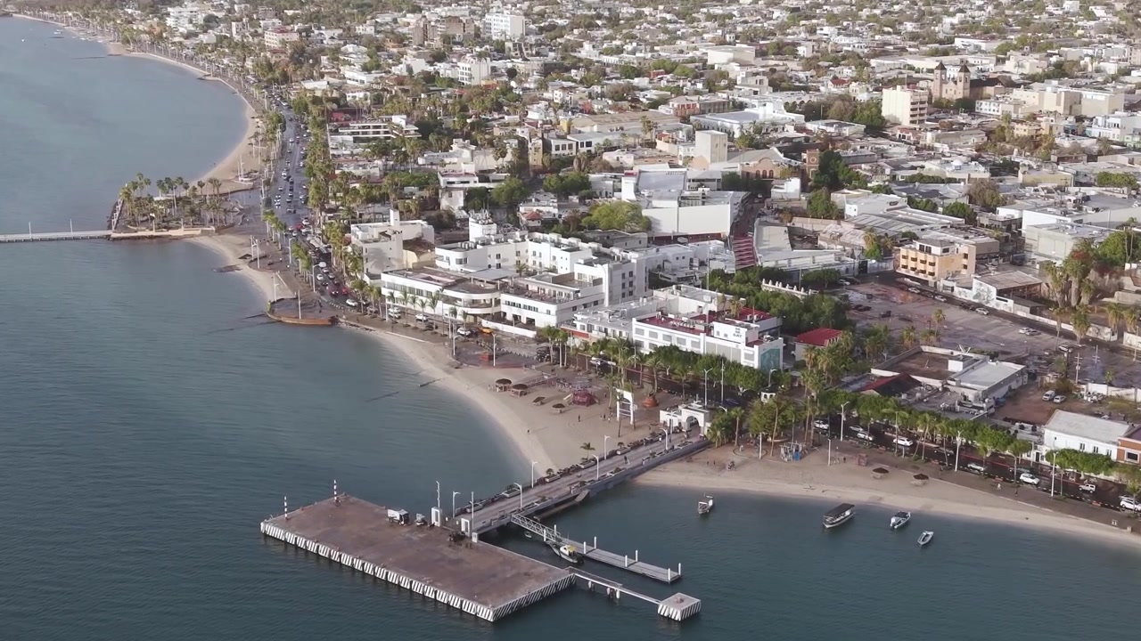 Una revelación cinematográfica con dron de ángulo alto mostrando la cuadrícula arquitectónica de La Paz fusionándose con el icónico Malecón