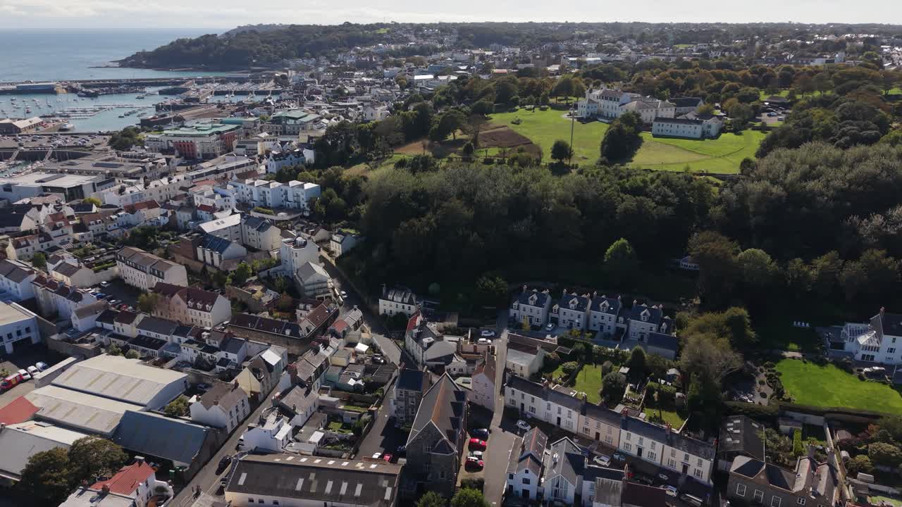 High drone footage over Les Cotils Christian Centre St Peter Port Guernsey and onwards above the roof tops of the town on bright but cloudy day with views across town the harbour and Havelet Bay