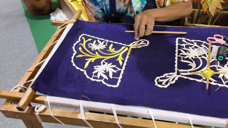 A skilled artisan performs traditional Malay Tekat embroidery. He meticulously sews gold thread onto rich velvet fabric. This rare, ancient craft represents a vanishing heritage art form