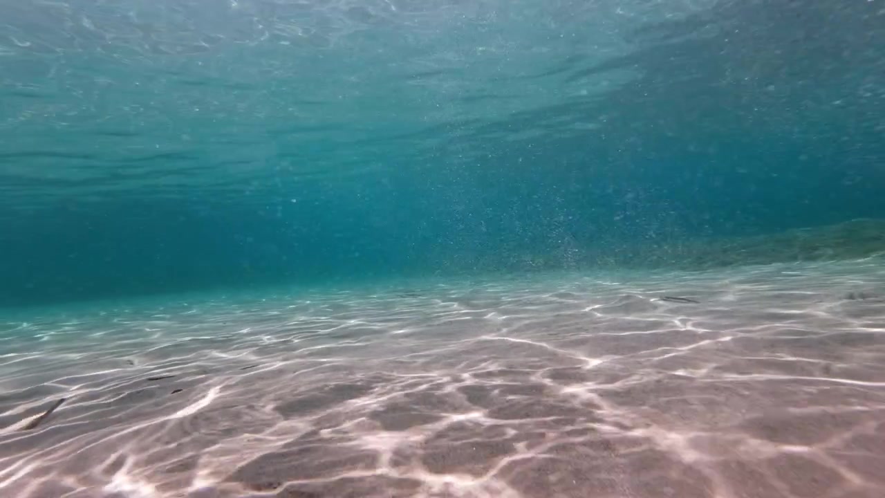 Nuvens de bolhas sobem acima de um leito marinho arenoso ondulado em águas rasas de cor turquesa perto de Santorini