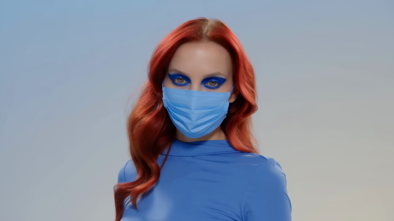 Junge Frau mit roten Haaren und blauem Augen-Make-up trägt medizinische Maske