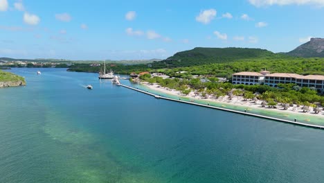 aerial dolly above boat channel with beach side resort behind pier, santa barbara beach curacao