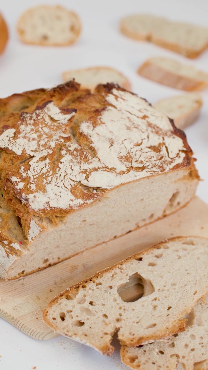 A hand picks up a slice of crusty sourdough bread from a wooden board.