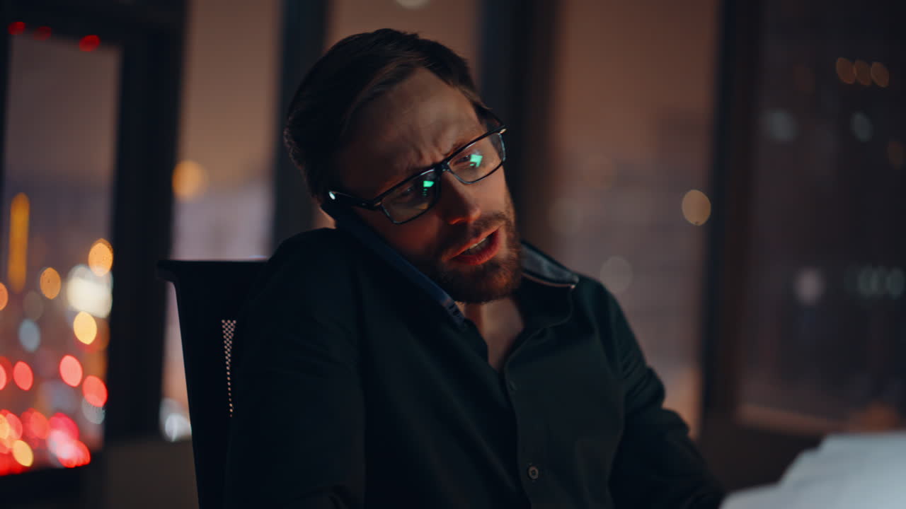 Ritratto di un libero professionista che parla al cellulare di notte in un ufficio remoto mentre legge dei documenti
