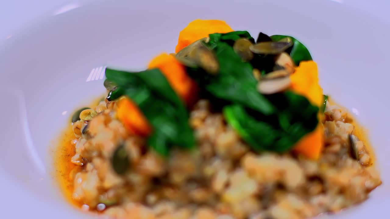 Nahaufnahme einer Gourmet-Grain-Bowl, angerichtet mit Kürbisstücken, Blattgemüse und gemischten Samen. Gesundes Restaurantgericht mit rustikaler Textur, warmen Farben und eleganter moderner Präsentation.