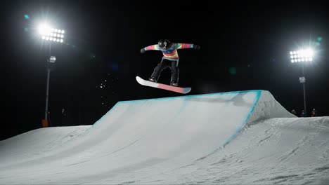 a snowboarder executes an impressive jump on a nighttime snow park slopestyle course, showcasing skill and courage under bright lights