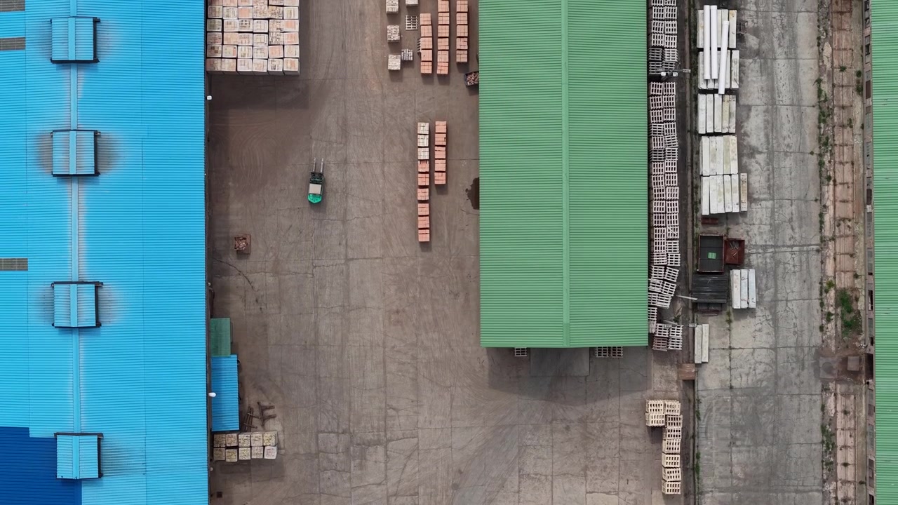 Una ripresa aerea mostra un piazzale industriale pieno di pile di materiali da costruzione e capannoni industriali, evidenziando la logistica moderna e le catene di approvvigionamento edili