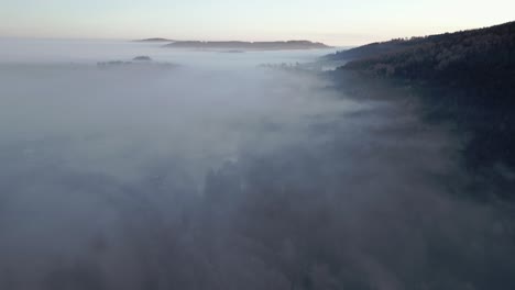 aerial view of hilly, serene landscape of a forested area enveloped in mist during early morning