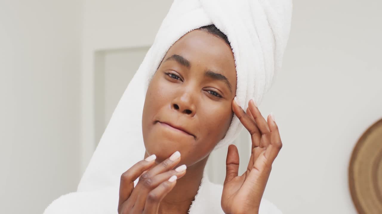 Video of happy african american woman in robe moisturizing face