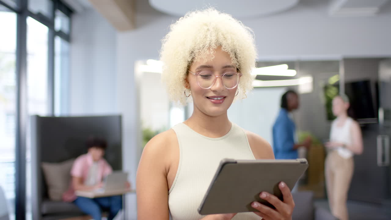 Using tablet, woman with curly hair smiling in modern office environment