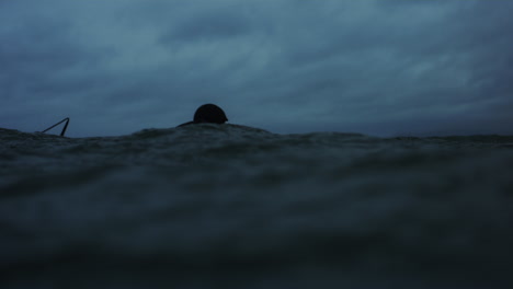 Tracking-pan-follows-surfer-in-full-wetsuit-paddling-through-stormy-ocean-water