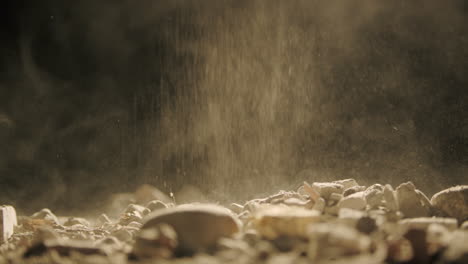 macro shot of falling dust and rocks on surface with black background, slow smooth dolly