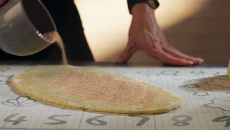 baker sprinkling cinnamon powder onto dough. making cinnamon rolls. closeup, sliding shot