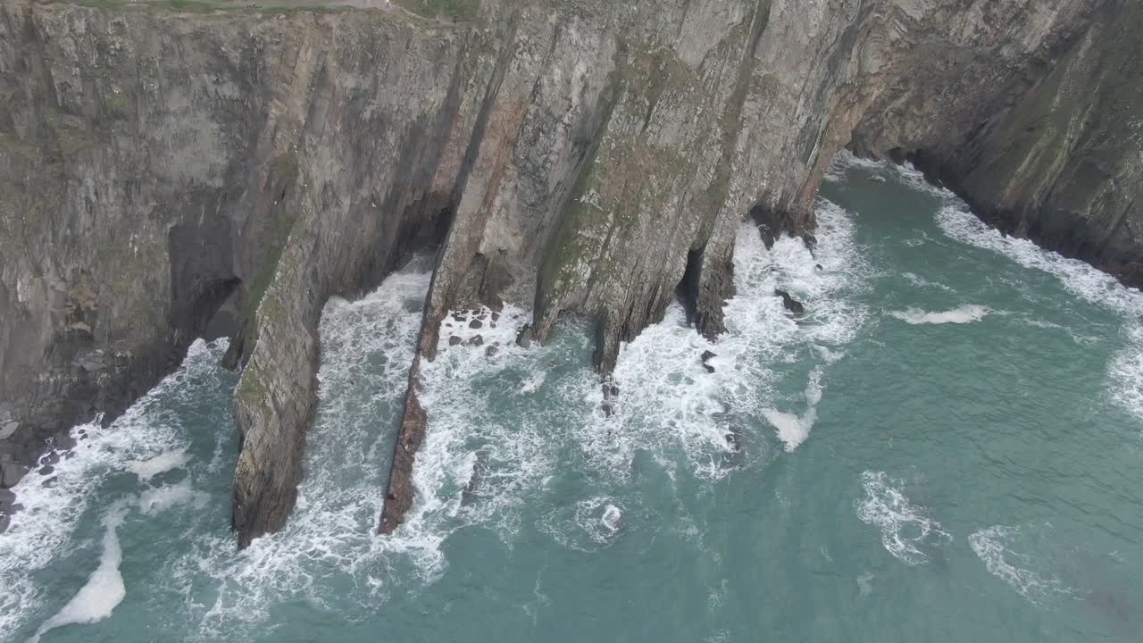 Slow aerial slide of irish sea side cliffs with rough seas and waves hitting the cliffs