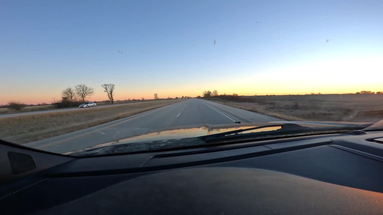 Punto di vista dal parabrezza mentre si guida su un'autostrada con poco traffico superando terreni agricoli e campi