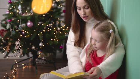 madre e hija sentadas en el suelo cerca del árbol de navidad 1