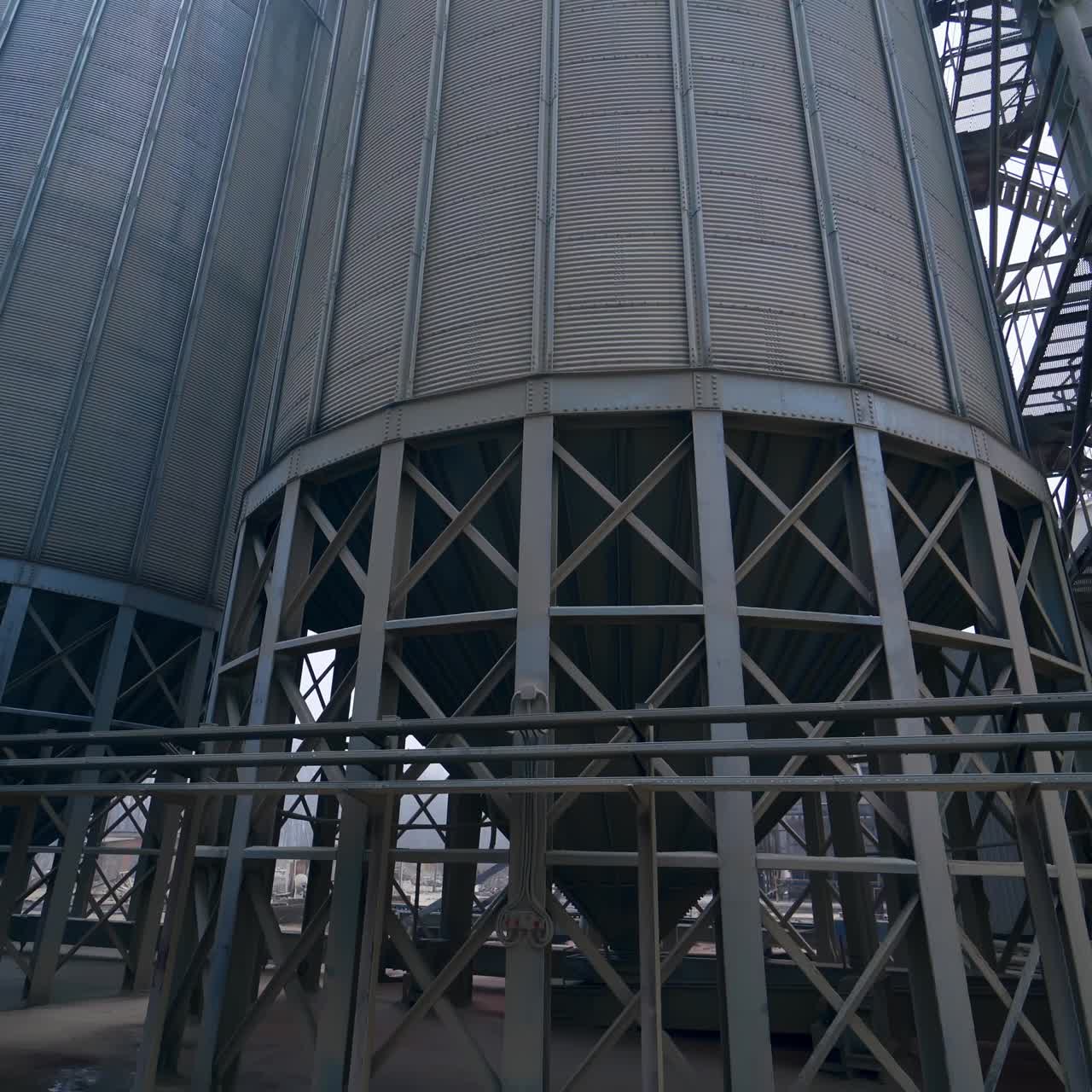 Huge steel tanks of grain silos standing on the massive metal supports. Moving closer to the basis of granary cisterns at the modern factory