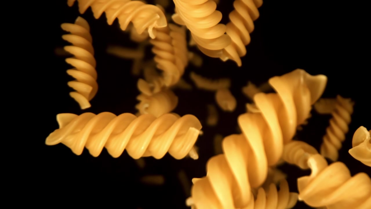 Pasta fusilli cruda che cade al rallentatore su sfondo nero