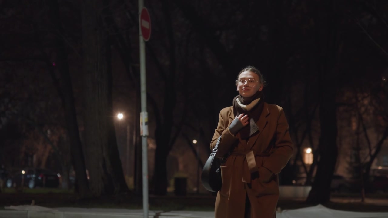 Marciapiede del parco di notte con un pendolare, uomo con cappotto marrone che si ferma vicino a un lampione controllando il telefono, respiro visibile nell'aria fredda, alberi silenziosi e panchine vuote, ritratto ravvicinato cinematografico, sguardo contemplativo