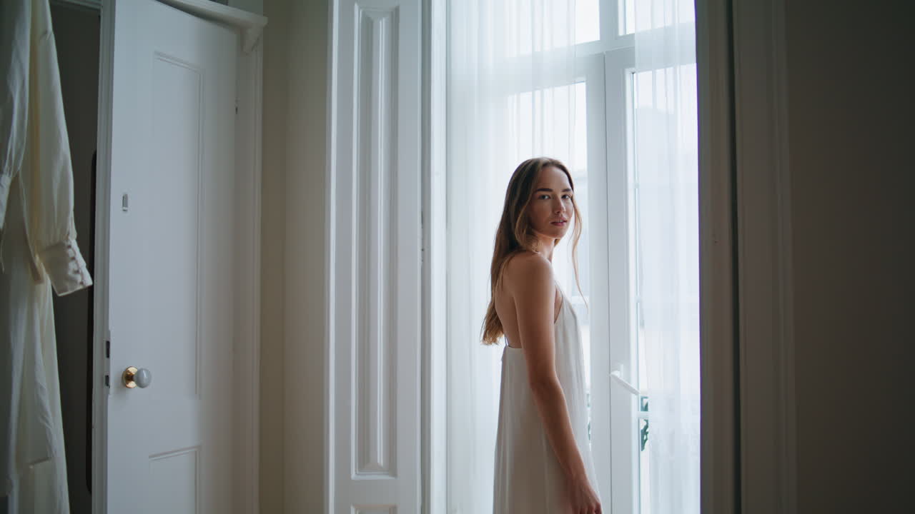 창문 인테리어에서 포즈를 취하는 부드러운 여성. 침실에서 휴식을 취하는 카메라를 찾는 여성