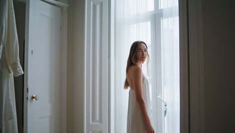 창문 인테리어에서 포즈를 취하는 부드러운 여성. 침실에서 휴식을 취하는 카메라를 찾는 여성