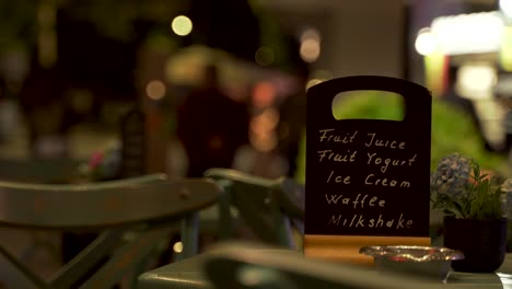 Menu-of-night-bar-on-pavement-with-people-walking-on-city-sidewalk-background