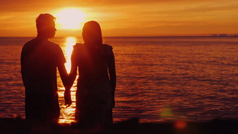 multi-ethnic couple in love holding hands on the background of the sea where the sun sets beautifull