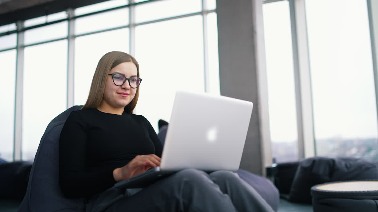 Beautiful young woman in casual clothing using laptop and smiling while working indoors