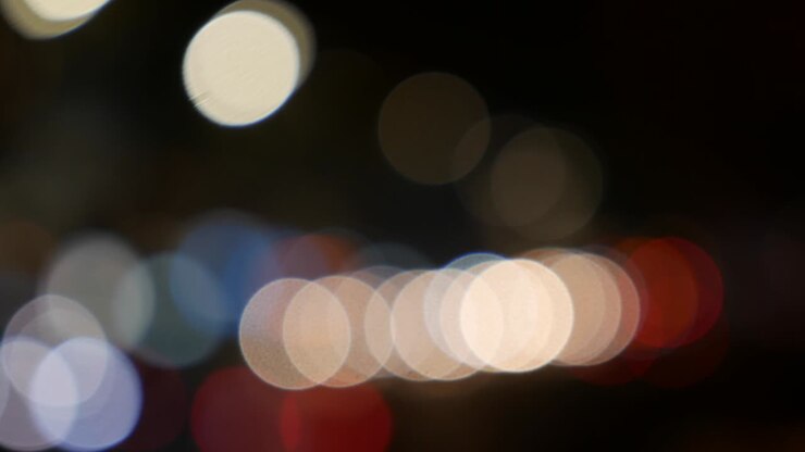 Beautiful glittering bokeh in dark blurry background at night. The round colorful bokeh shine from car lights on city street. Out of focus with blurry. Unfocused city lights. Traffic bokeh. Abstract concept