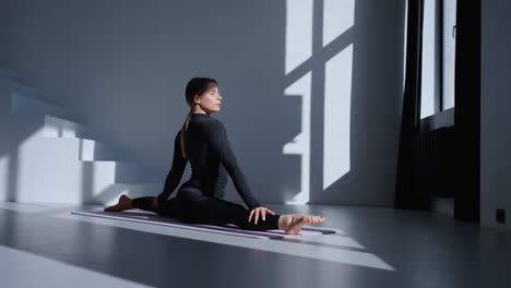 woman doing yoga splits on a mat in a studio